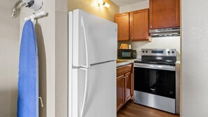 Cocina compacta con refrigerador blanco, microondas, horno, gabinetes de madera y una lámpara.