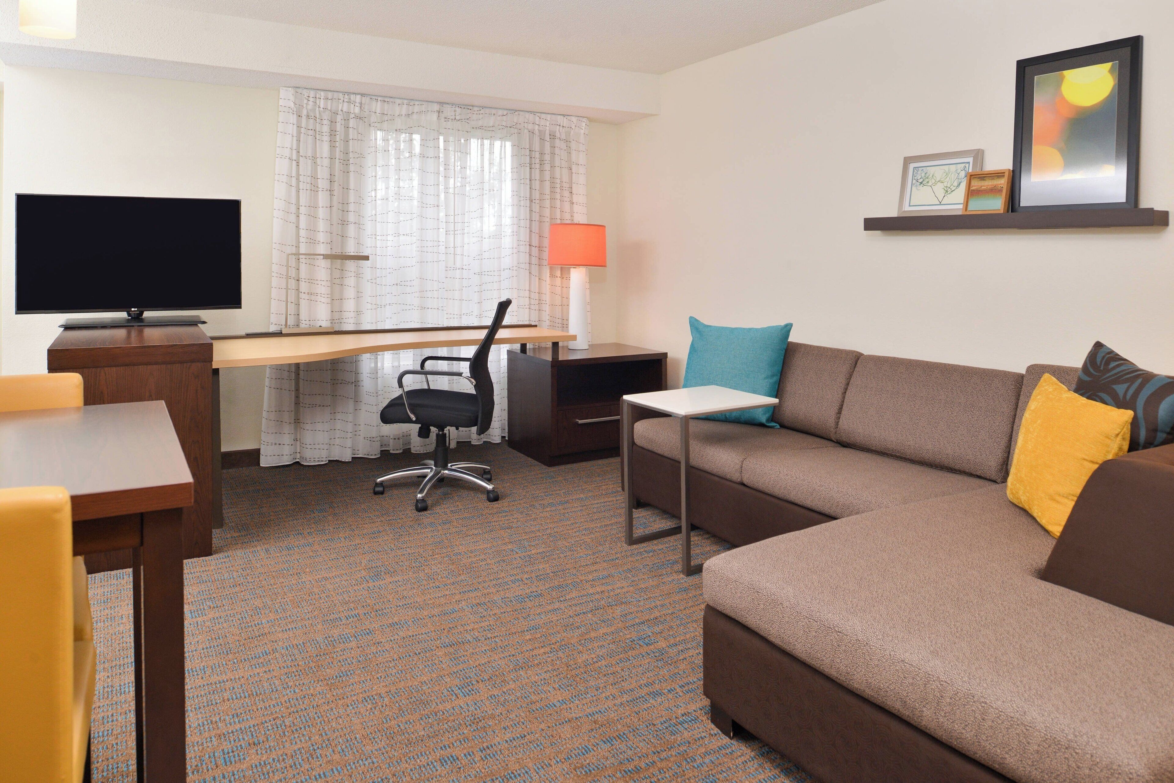 Habitación de hotel con televisión de pantalla plana, escritorio, sofá y lámpara.