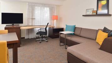 Habitación de hotel con televisión de pantalla plana, escritorio, sofá y lámpara.