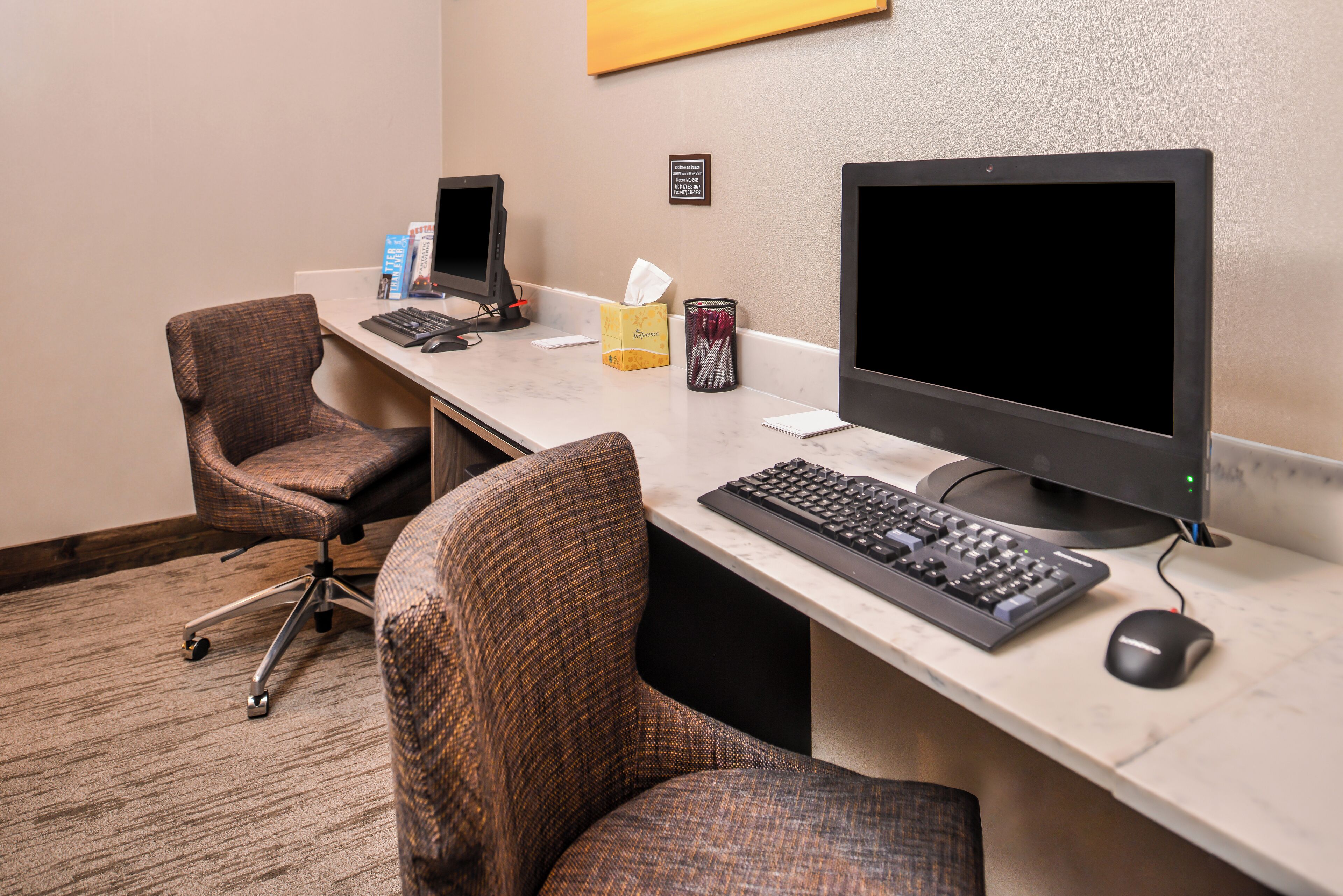 Un espacio de trabajo de hotel con dos monitores de computadora, un teclado y un ratón sobre un escritorio de mármol.