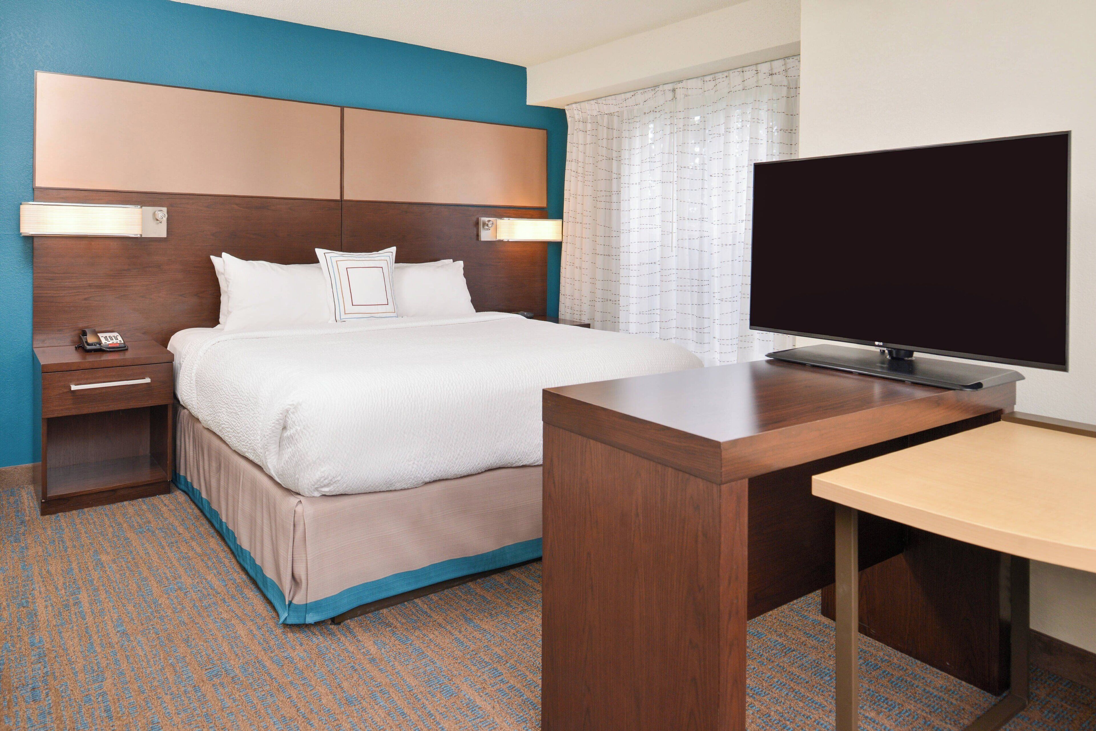 A hotel room with a bed, a desk, a television, a nightstand, and a telephone.