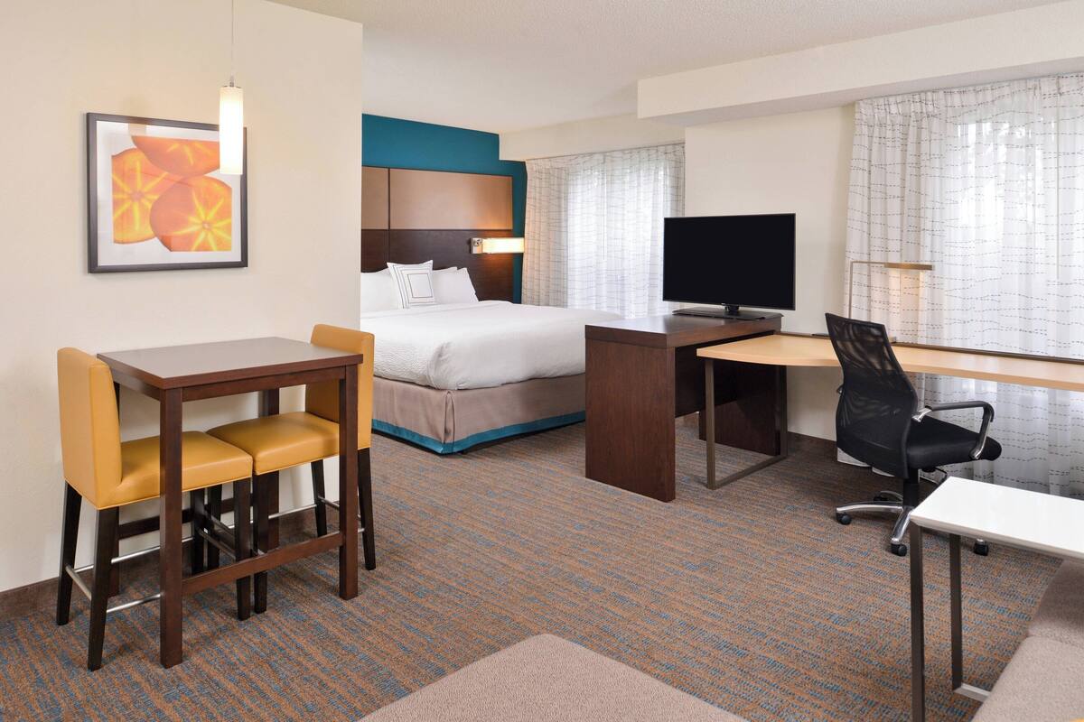 A hotel room with a bed, a desk, a chair, a television, and a framed picture on the wall.