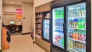 Vestíbulo de hotel con máquinas expendedoras llenas de bebidas, un mostrador de recepción y un monitor de ordenador.