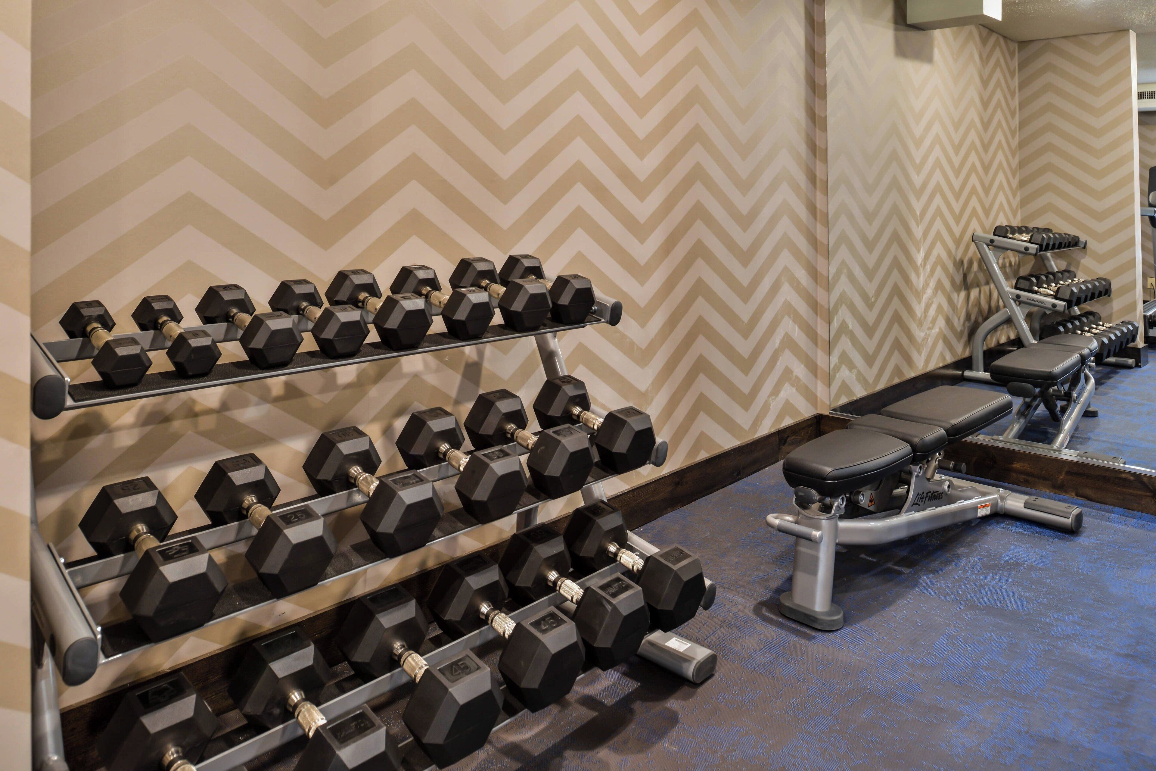 A gym with hexagonal dumbbells on racks, a bench, and a rowing machine.