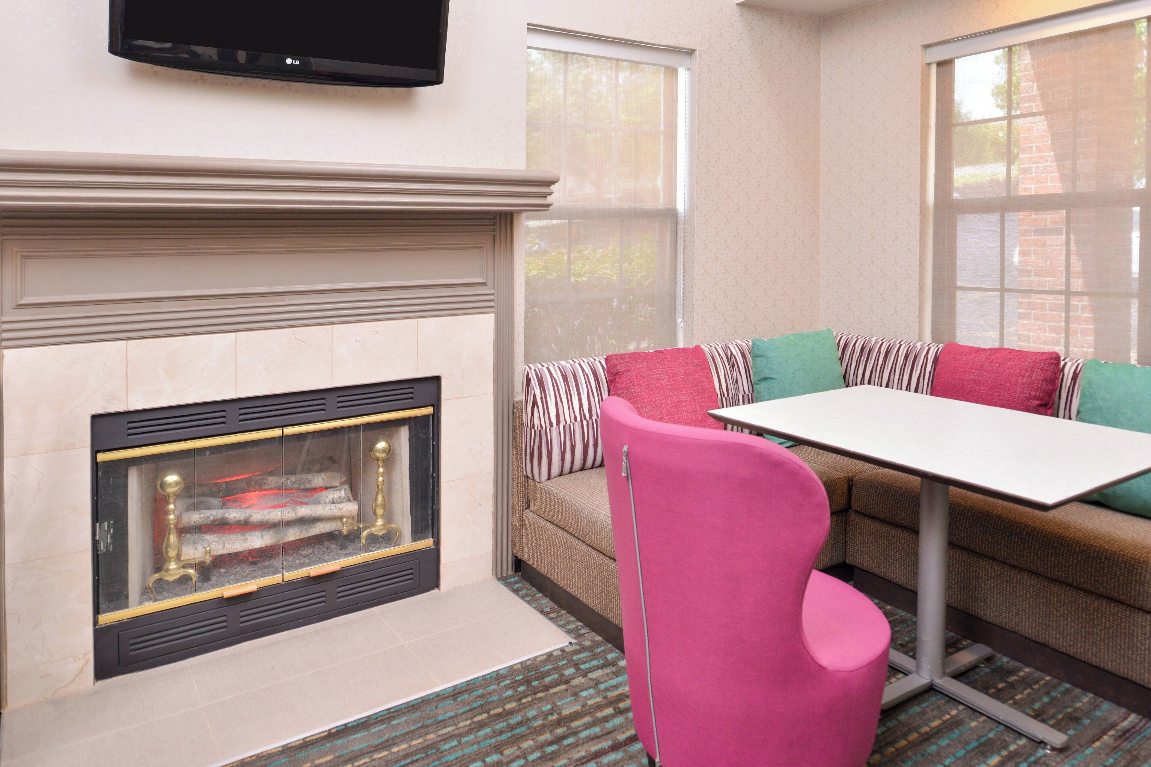 A cozy living area with a fireplace, a sofa with striped cushions, a pink chair, and a table.