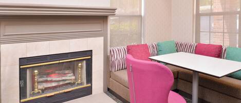 A cozy living area with a fireplace, a sofa with striped cushions, a pink chair, and a table.