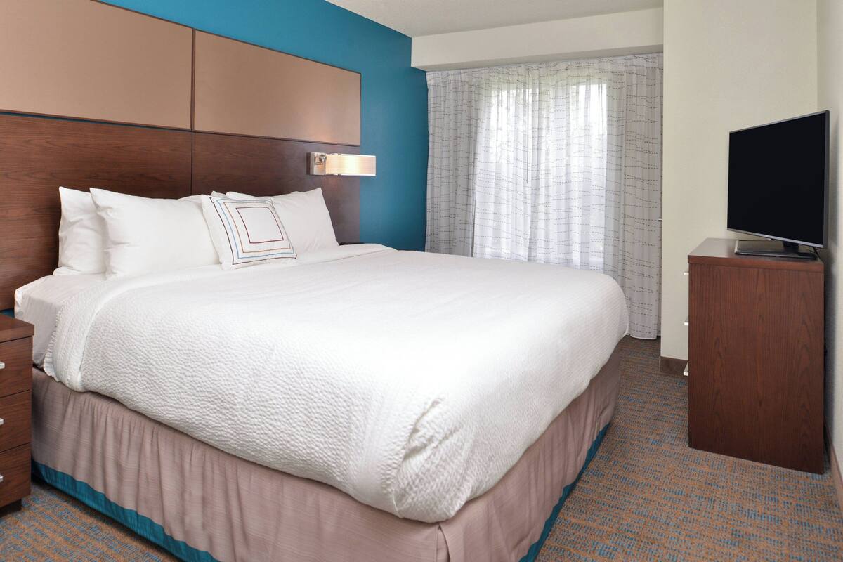 A hotel room with a large bed, a wooden headboard, a flat-screen TV, and a window with curtains.