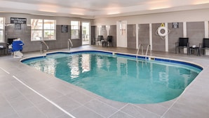 Una piscina con una silla de salvavidas, un cartel que indica que no hay salvavidas de servicio y varias sillas de descanso.