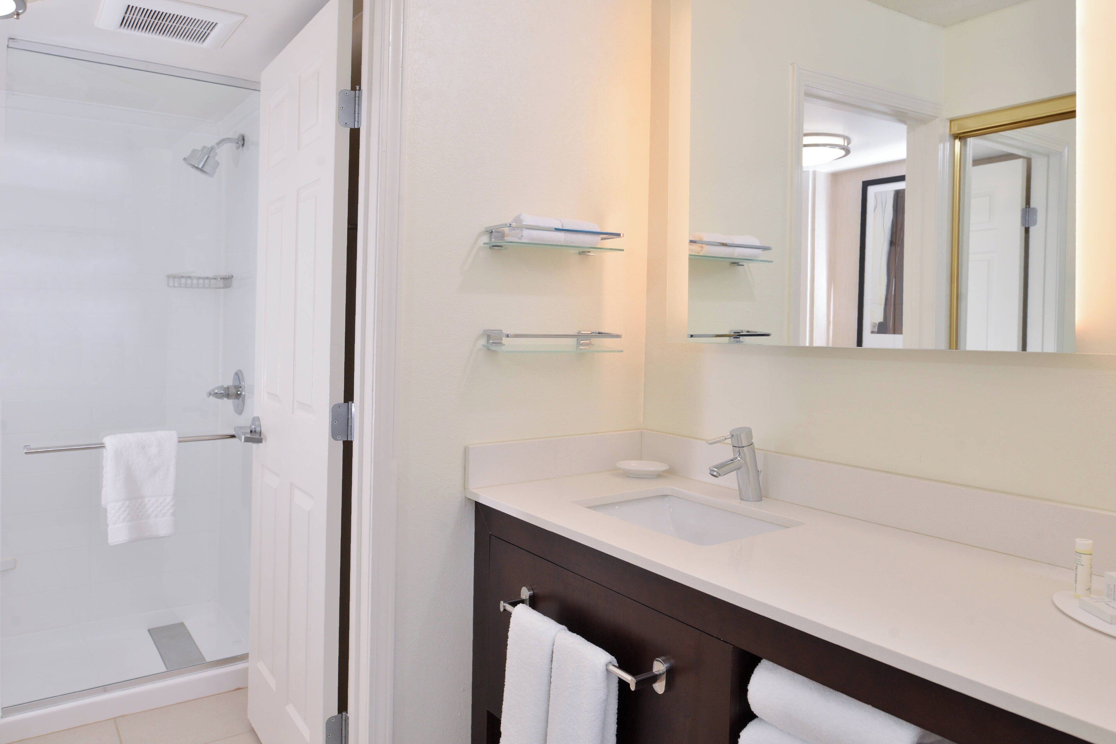 A modern bathroom with a glass shower enclosure, a white sink, and a dark vanity.