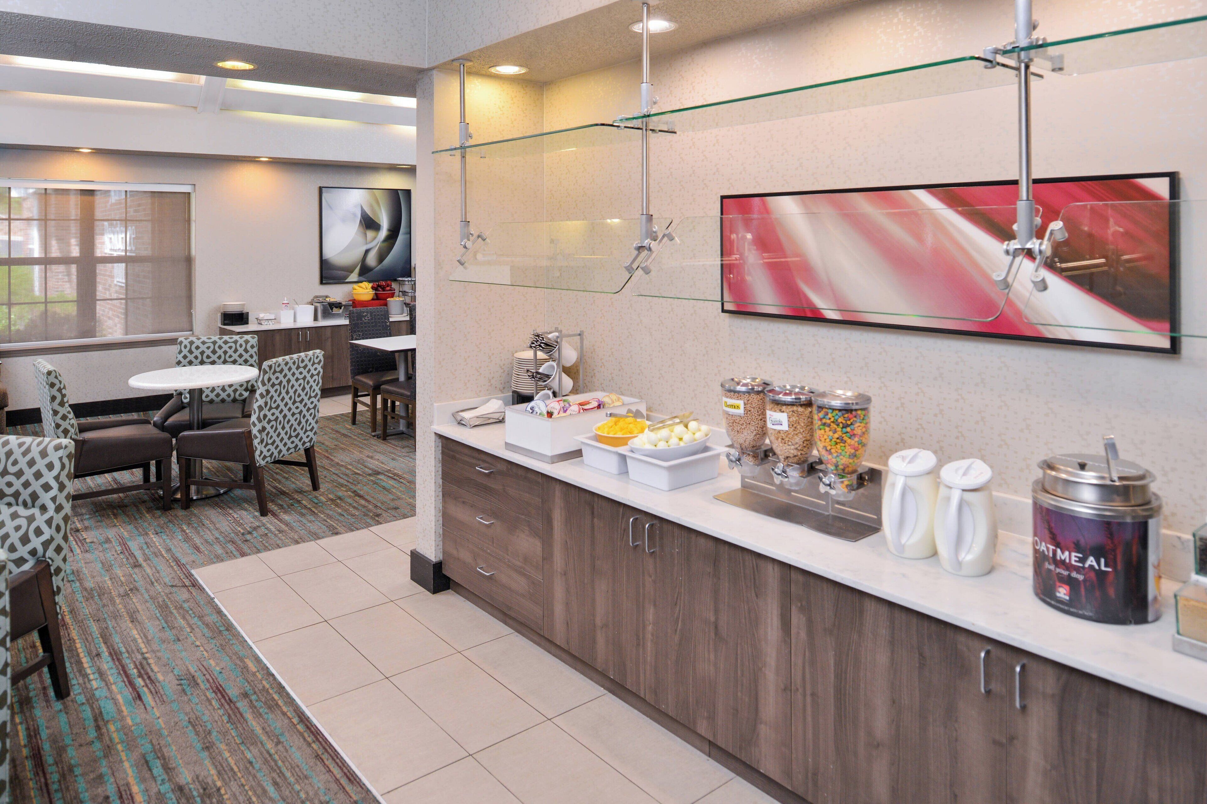 A hotel breakfast area with a counter, seating, and a large abstract painting on the wall.