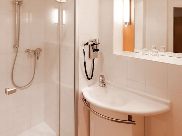 A bathroom with a glass-enclosed shower, a white sink with a chrome faucet, and a mirror above the sink. - ibis Nuernberg Altstadt (Nuremberg)