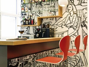 A bar area with a counter, shelves with bottles, glasses, and a mural. - ibis Nuernberg Altstadt (Nuremberg)