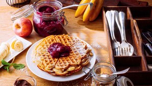 A plate of waffles with fruit compote and powdered sugar, a jar of chocolate spread, and a jar of sprinkles on a wooden table. - ibis Nuernberg Altstadt (Nuremberg)