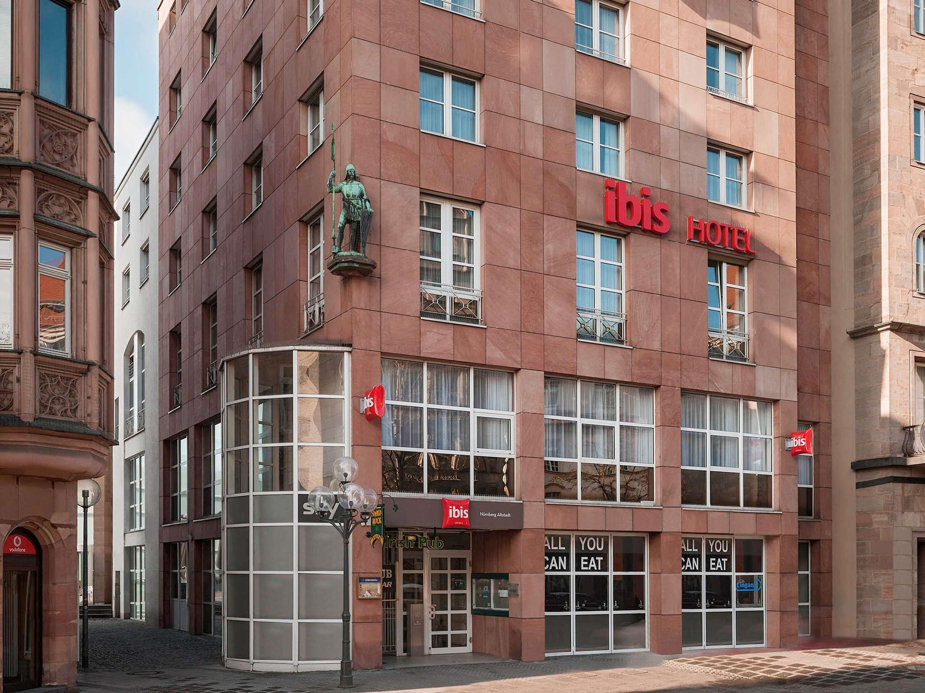 Ein Hotel mit rotem Schild, großen Fenstern und einer Statue an der Ecke.