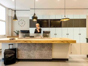 A reception desk with a modern design, a clock on the wall, and a large window providing natural light. - ibis Nuernberg Altstadt (Nuremberg)