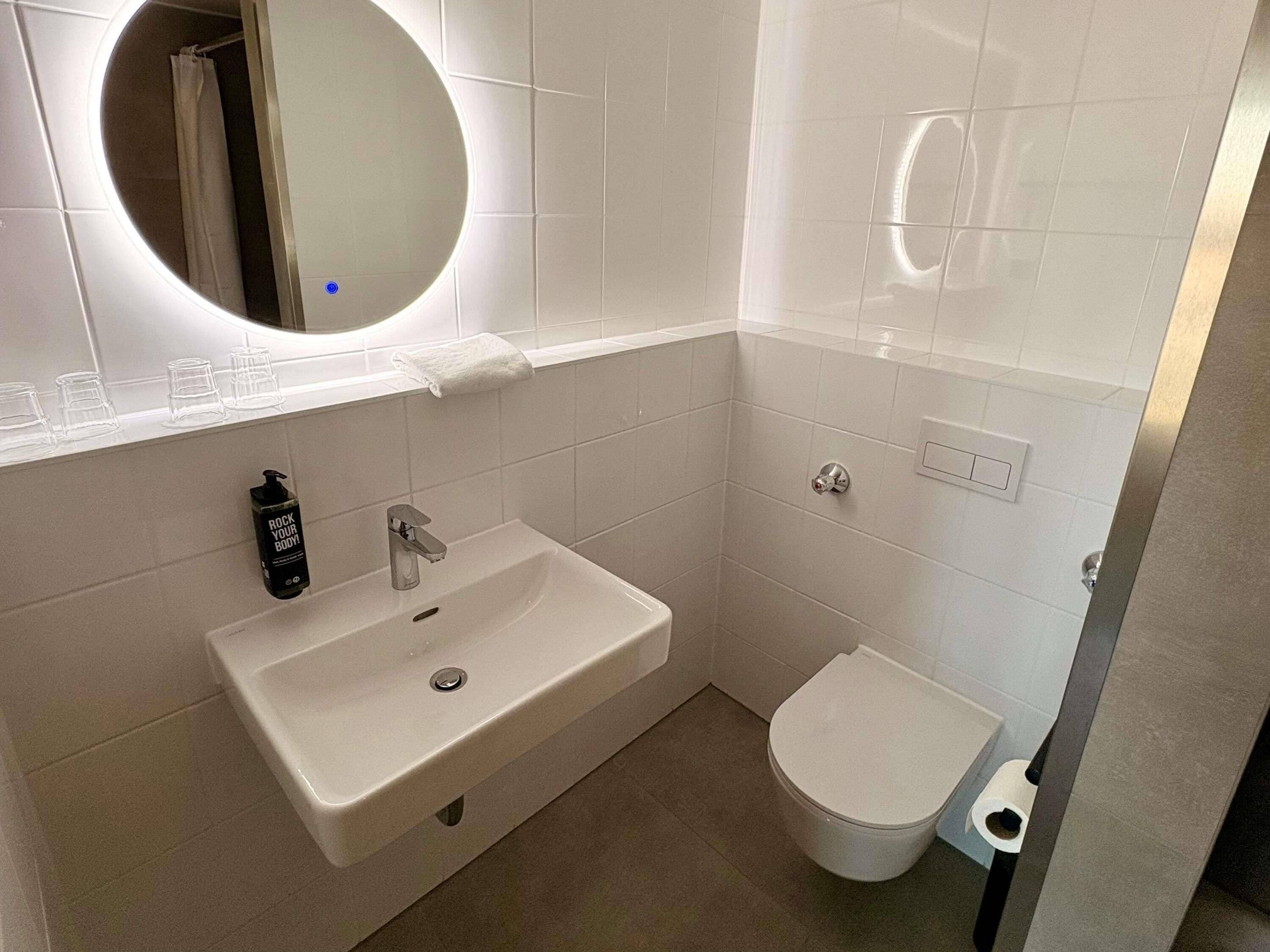 A modern bathroom with a white sink, a mirror, and a toilet.