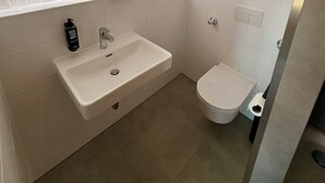 A modern bathroom with a white sink, a round mirror, a toilet, and a shower area. - ibis Nuernberg Altstadt (Nuremberg)
