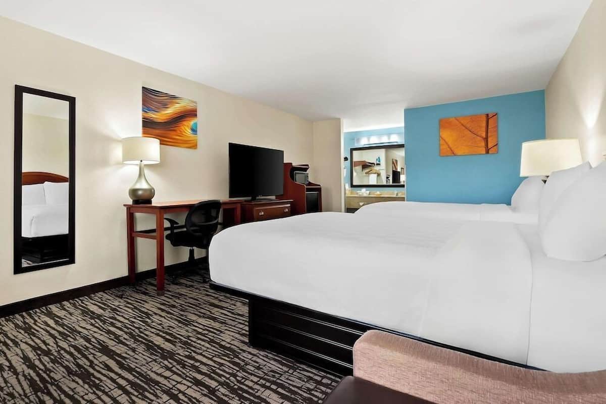 A hotel room with a large bed, a desk with a television, a mirror, and artwork on the walls.