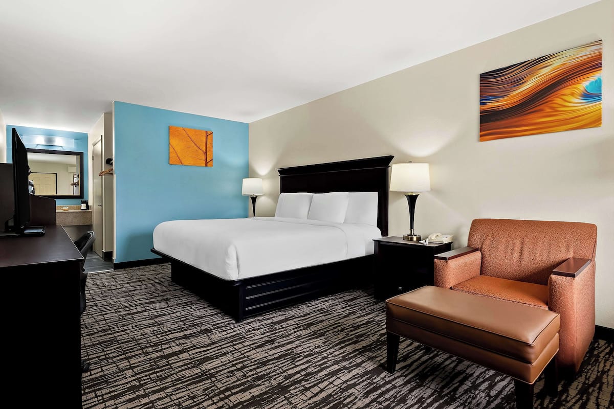 A hotel room with a bed, a chair, a desk, and a nightstand.