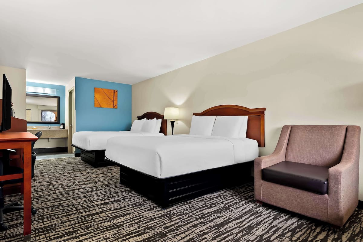 A hotel room with two beds, a desk, a chair, and a TV.