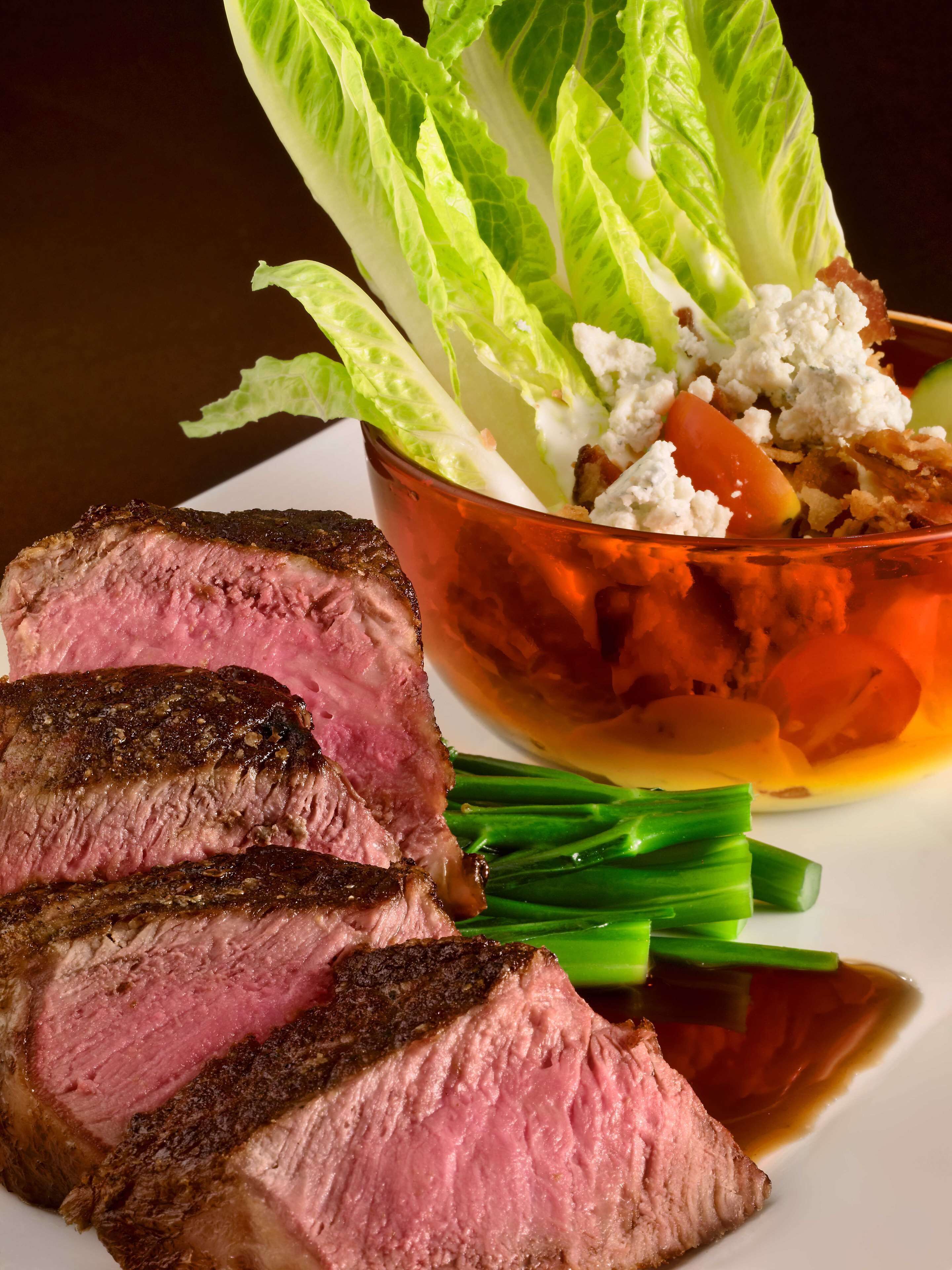 A plate with sliced steak, a bowl of salad, and green vegetables.