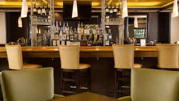 Una zona de bar con varios taburetes y una barra repleta de botellas y vasos.