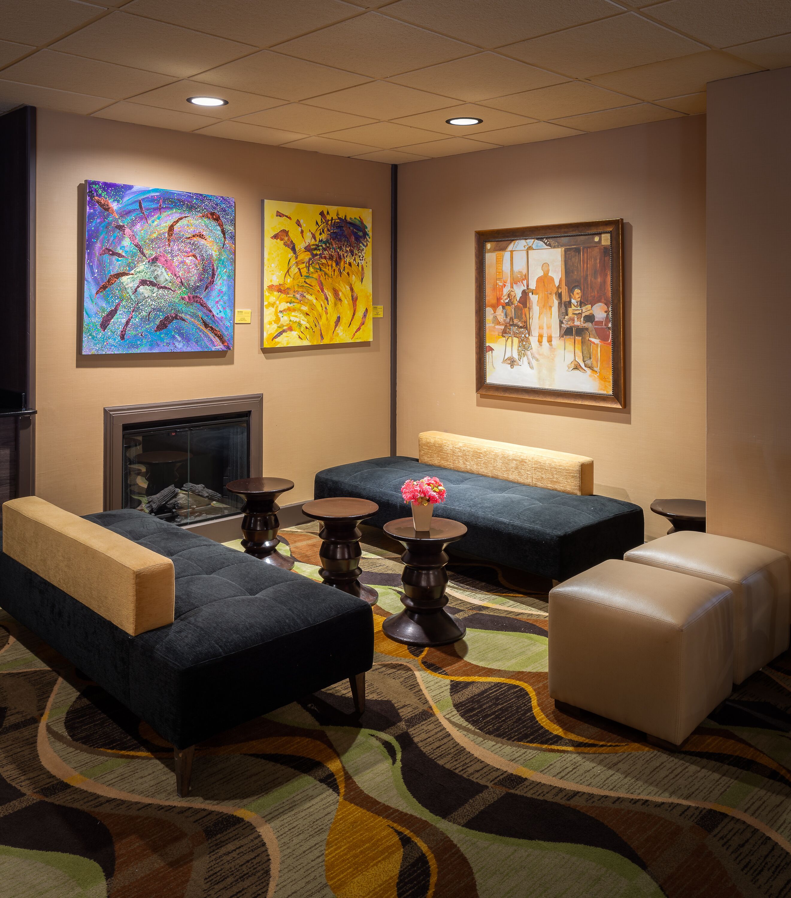 A hotel lobby with seating, artwork on the walls, a fireplace, and a patterned carpet.