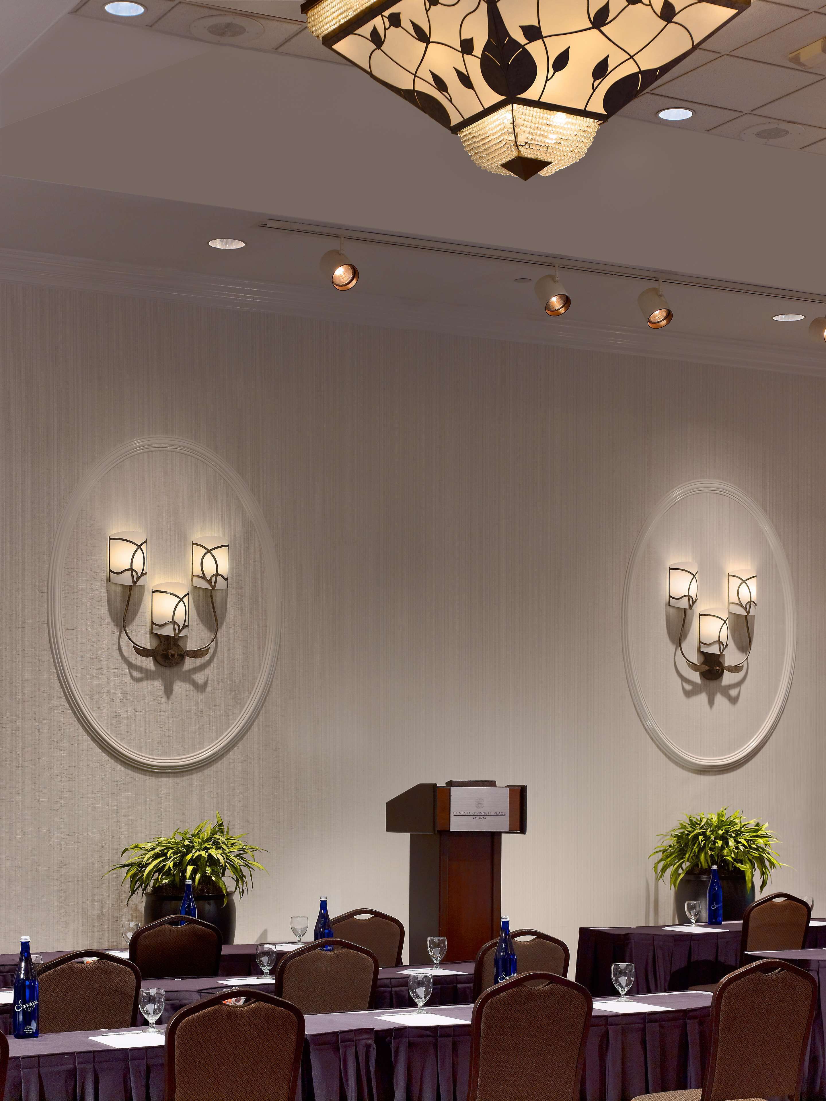 A conference room with a podium, round tables, chairs, and wall sconces.