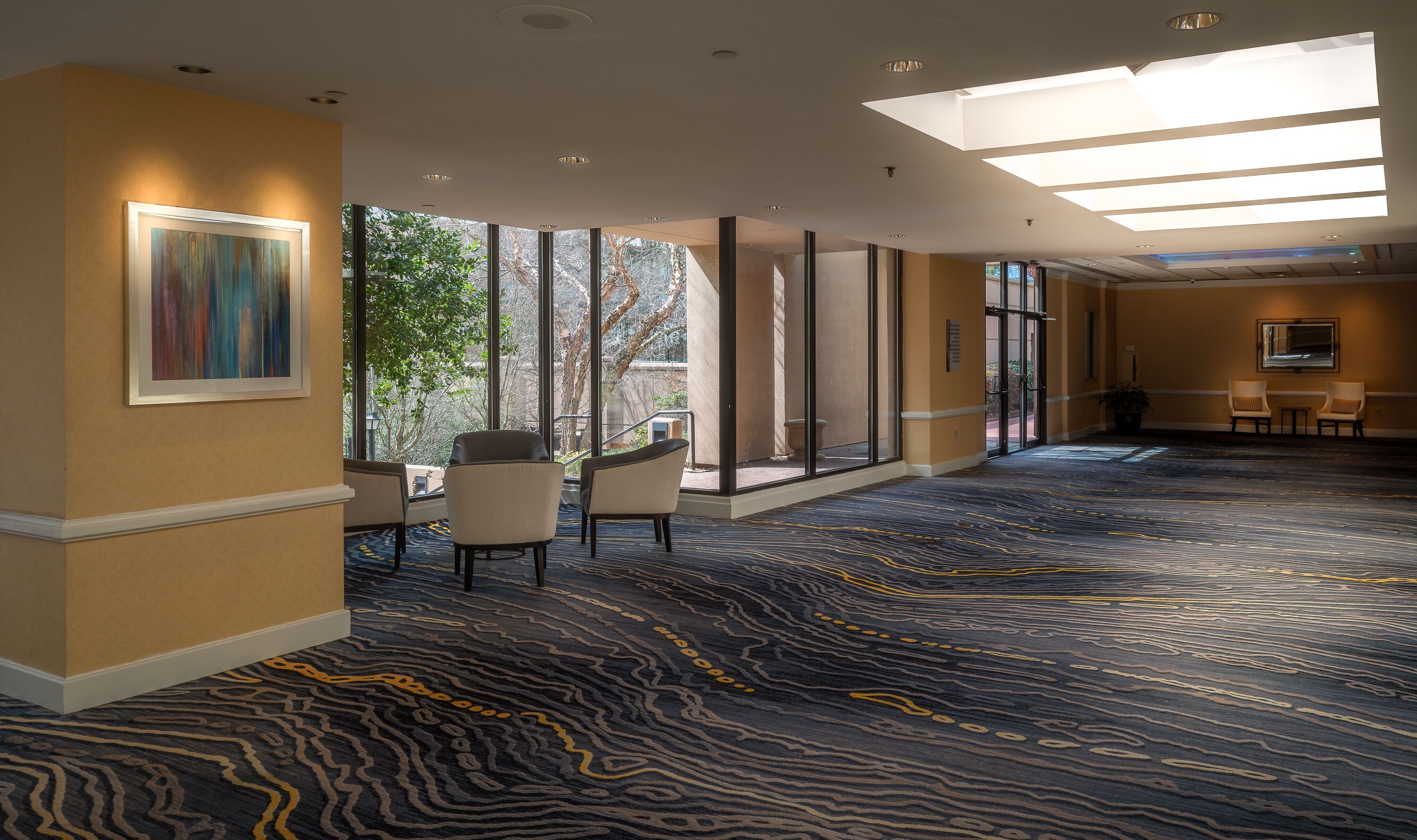 Un hall de hotel con alfombra estampada, ventanas amplias y zonas de descanso.