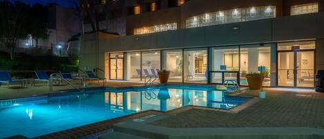 A hotel with a swimming pool, outdoor seating, and a well-lit entrance.