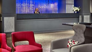 Un espace d’accueil avec un mur éclairé en bleu, deux chaises rouges, un fauteuil gris et un tabouret en osier.
