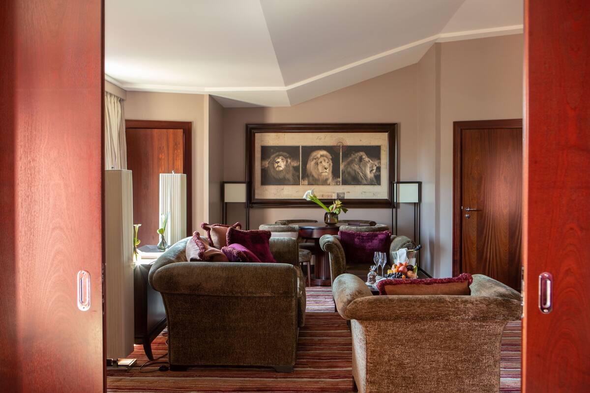 A living room with a sofa, armchairs, a coffee table, and a dining area with a table and chairs. There is a framed picture on the wall and a vase with flowers on the coffee table.