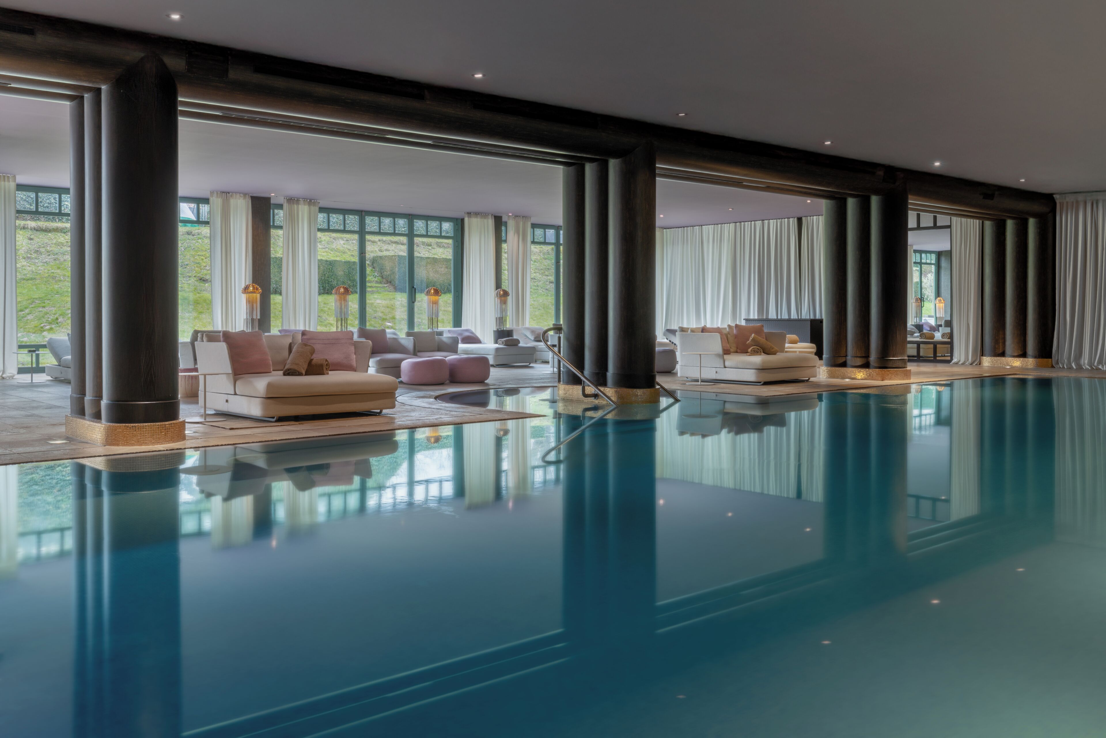 A spacious indoor swimming pool with multiple seating areas and large windows.