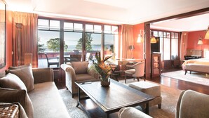 A hotel room with a large window, a dining area, a sofa, a coffee table, and a bed.