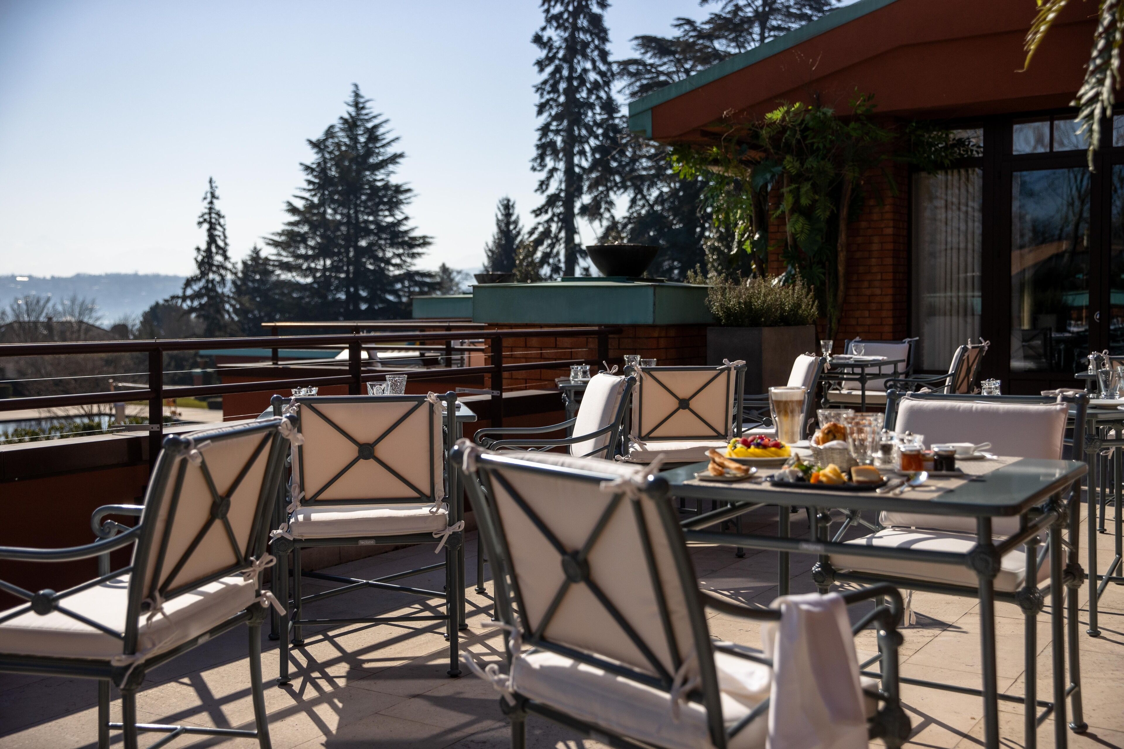 An outdoor patio with tables and chairs, a view of the city, and a building with a brick facade.