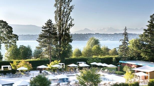 A resort with a pool area, lounge chairs, umbrellas, and a view of the water and mountains.