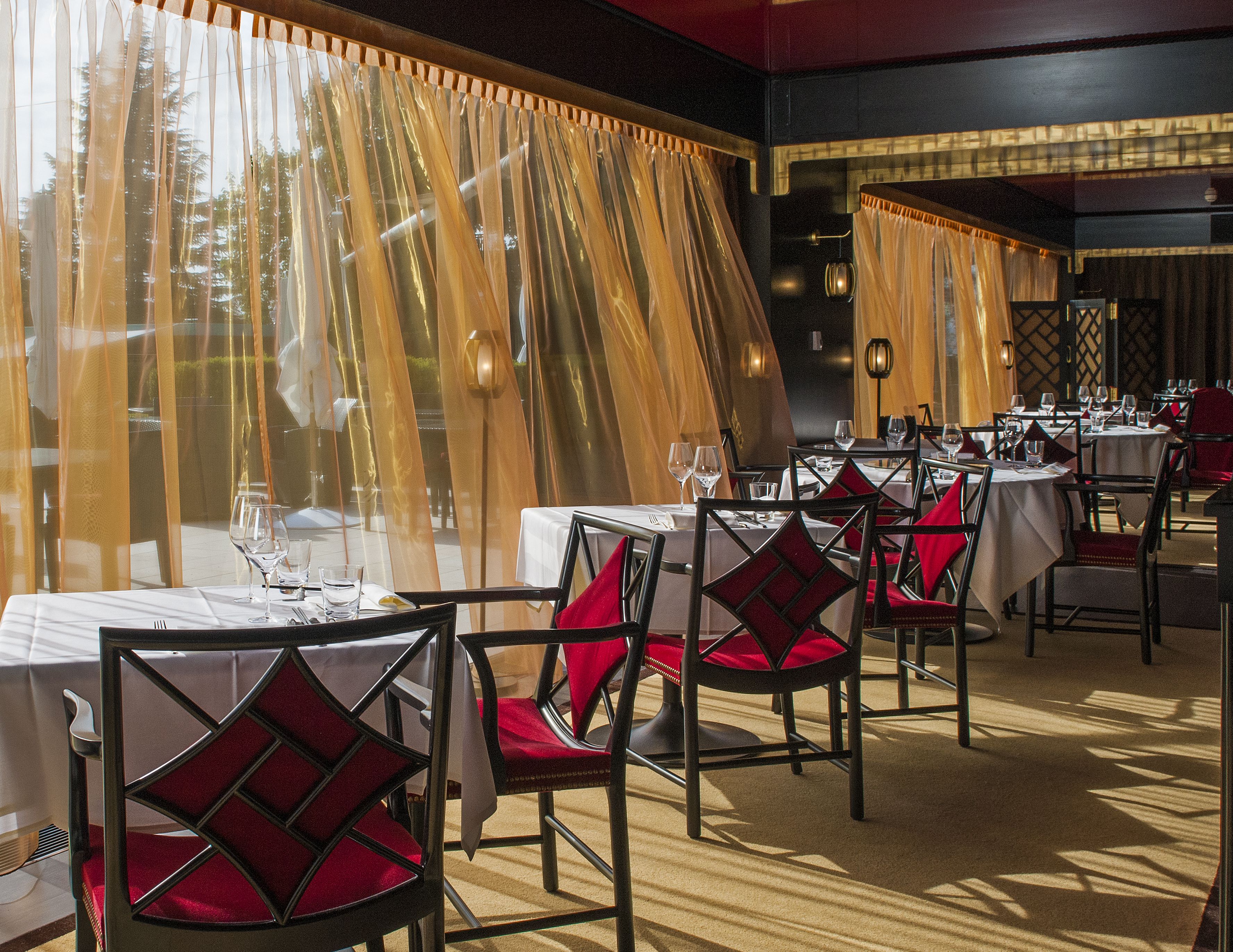 A restaurant with tables set for dining, featuring red upholstered chairs and white tablecloths.