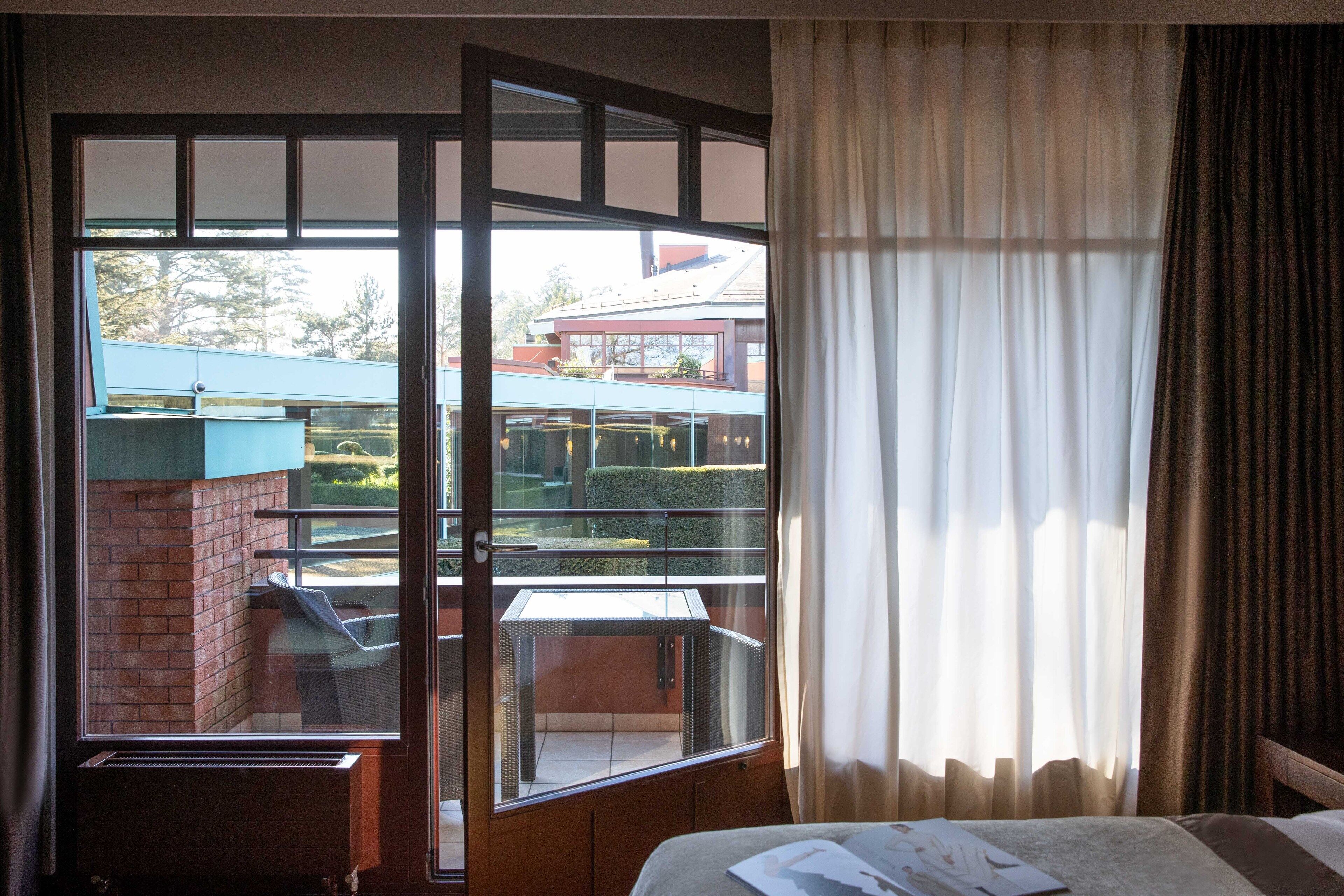 Habitación de hotel con una ventana grande, una cama y vistas a un edificio con techo azul y un balcón.