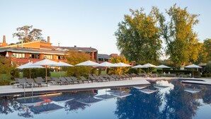 A swimming pool with lounge chairs and umbrellas, surrounded by trees and buildings.