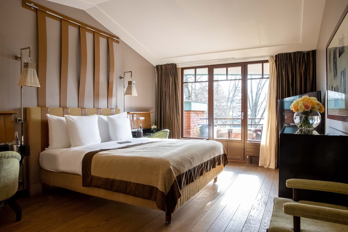 A hotel room with a large bed, a desk, a chair, a TV, and a window with curtains.