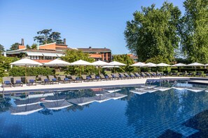 Une piscine entourée de verdure et de bâtiments, avec des chaises longues et des parasols.