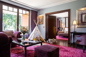 A hotel room with a large window, a red carpet, a sofa, a table with a vase of flowers, a teddy bear, a toy car, and a tent. - La Reserve Geneve Hotel and Spa (Bellevue)