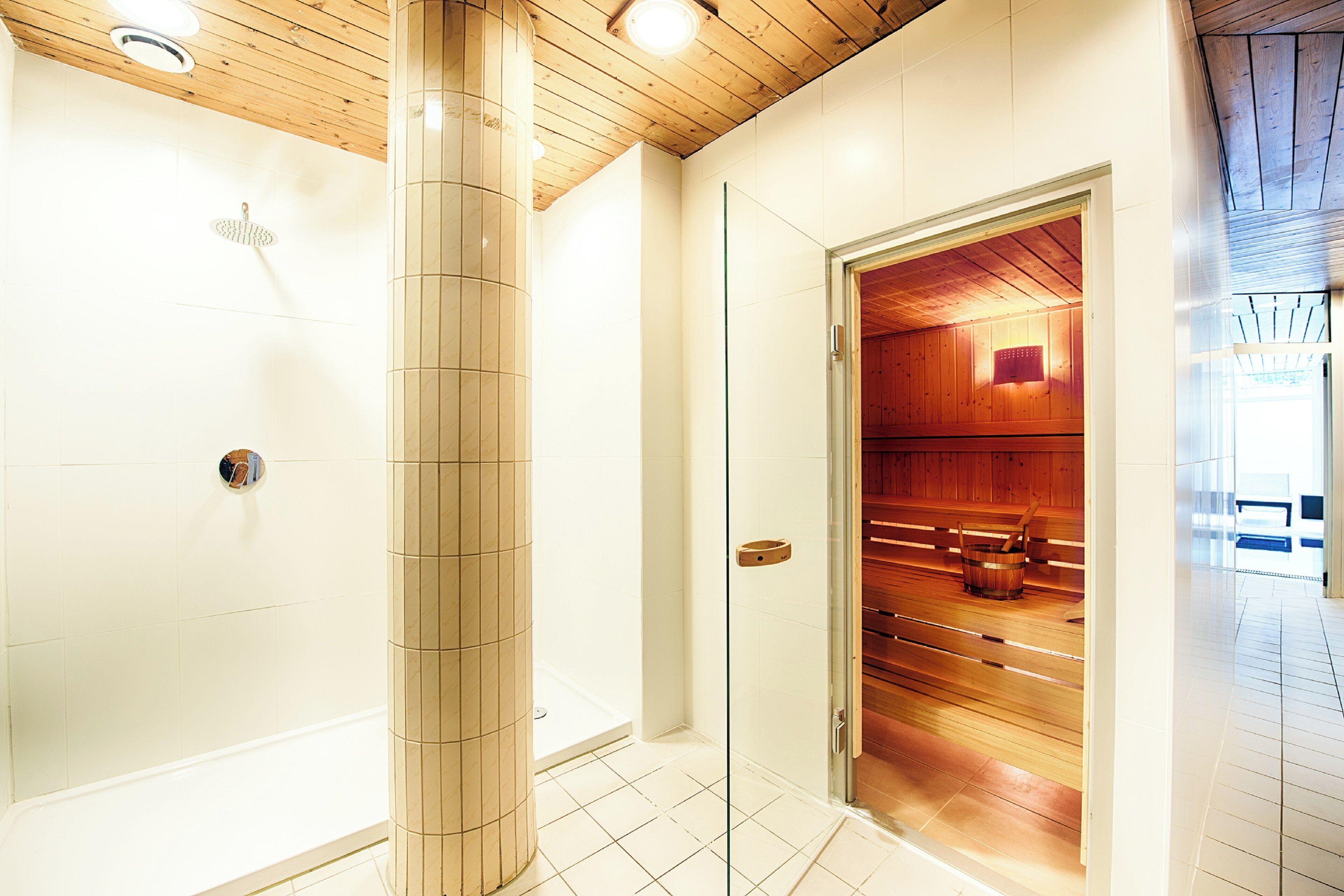 Une salle de bain moderne avec une douche à parois de verre, un banc en bois et un sauna visible à travers une porte ouverte.