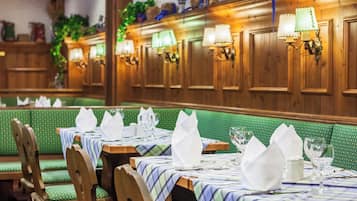 L’intérieur d’un restaurant est agrémenté de boiseries, de banquettes recouvertes d’un tissu vert et de tables dressées avec des serviettes blanches et de la verrerie élégante.