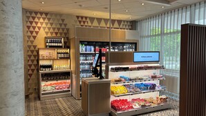 A modern retail space with a herringbone patterned floor, a digital screen displaying a greeting, and shelves stocked with various products. - Holiday Inn Munich - South by IHG (Munich)