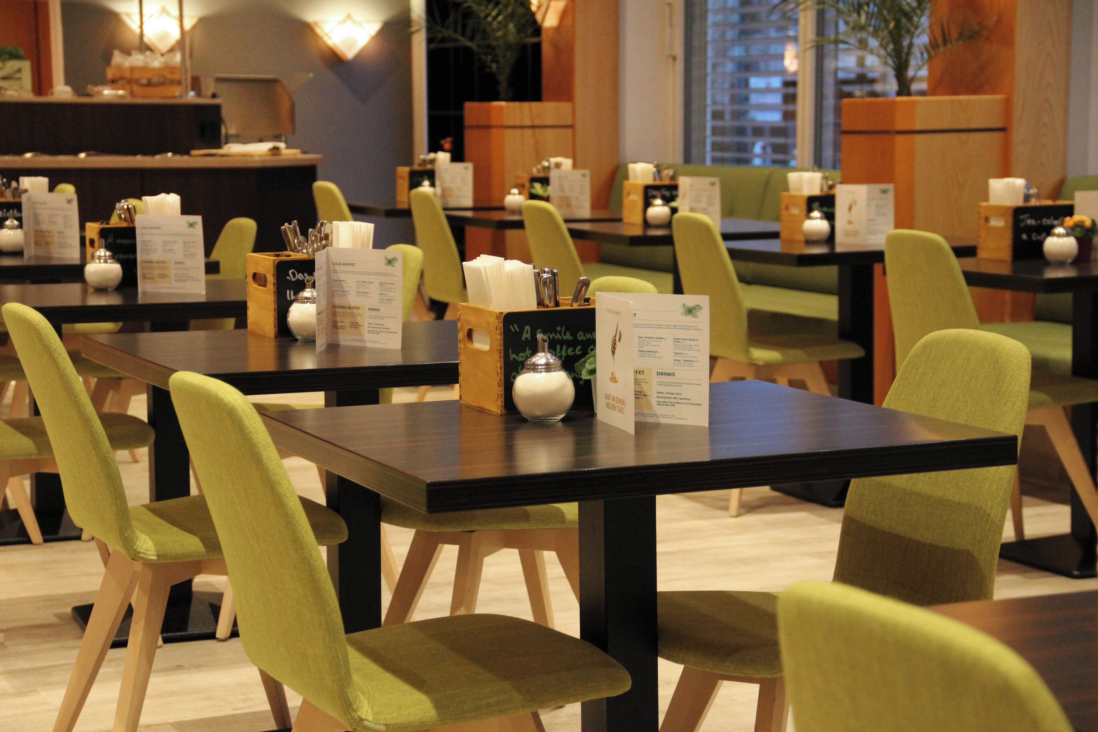 A restaurant with multiple tables and chairs, menus, and a chalkboard menu board.