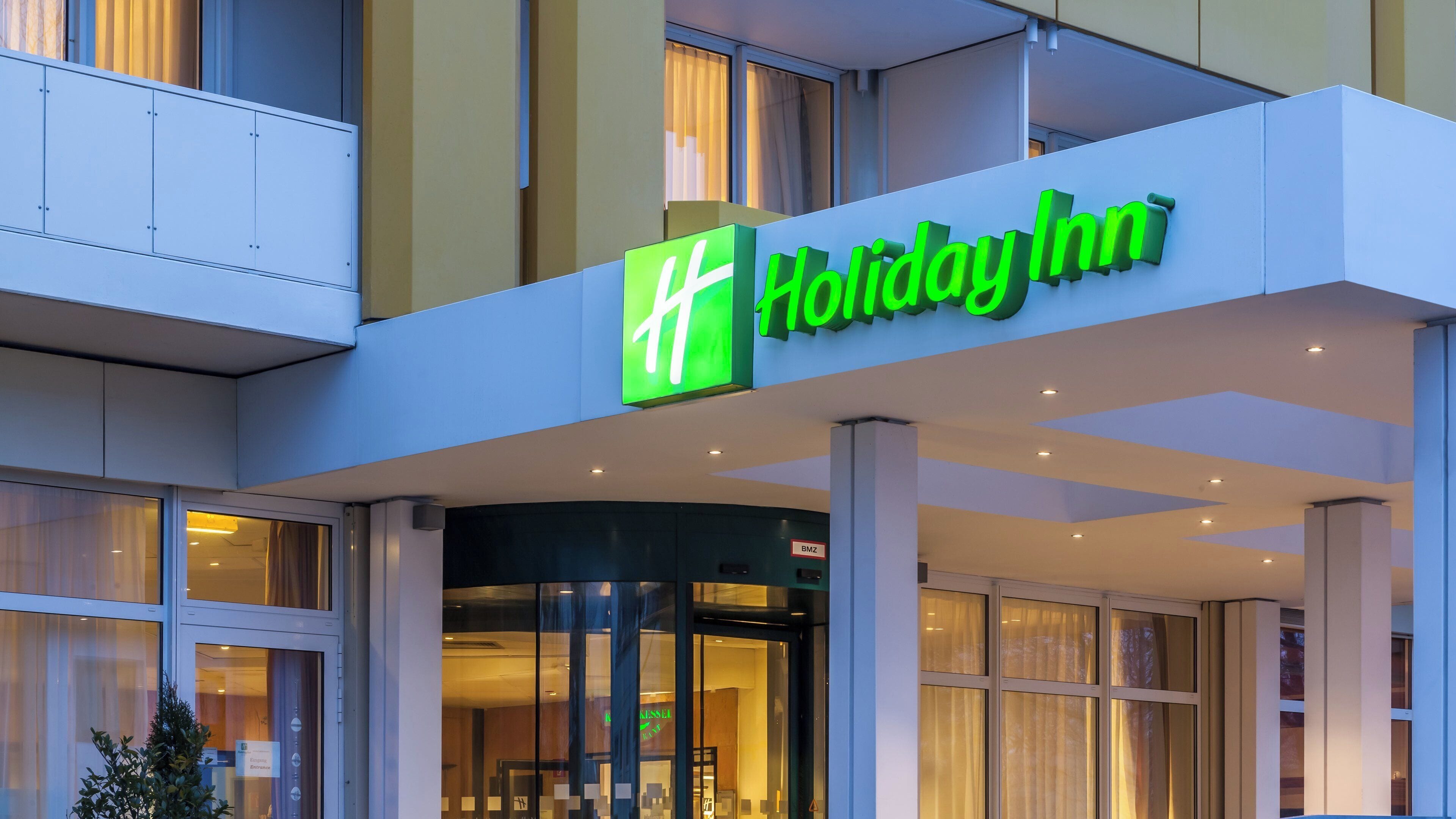 Eingangsbereich eines Holiday Inn Hotels mit auffälliger Beschilderung, Glastüren und einem gut sichtbaren Eingangsschild.