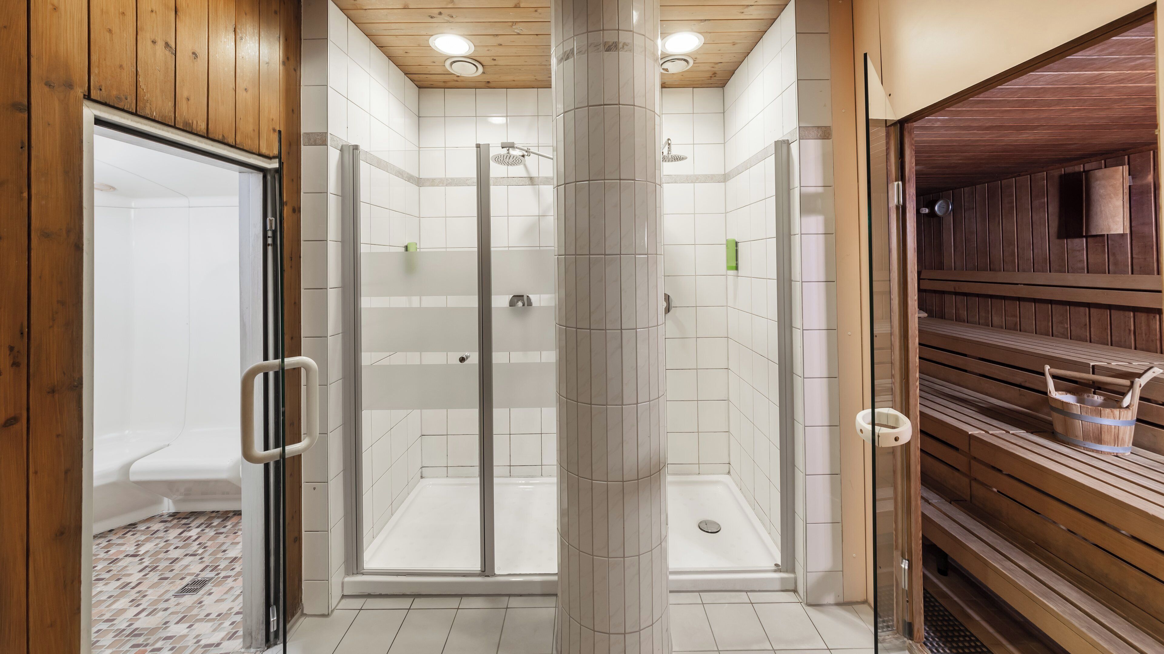 A modern bathroom with a glass shower enclosure, wooden benches, and a tiled floor.