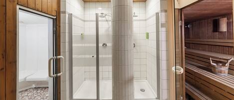 A modern bathroom with a glass shower enclosure, wooden benches, and a tiled floor.