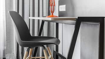 Een moderne bureaustoel met houten poten, een zwarte zitting en een houten rugleuning, geplaatst voor een bureau met een wit blad en een oranje lamp.